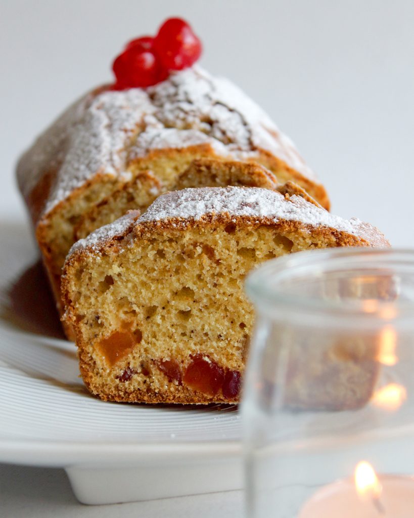 Un plum-cake speziato, natalizio, sistemato su un piatto bianco,vicino a una candela. Ricetta creata da Paola Uberti, digital food creator per il Cliente Tutte le Spezie del Mondo