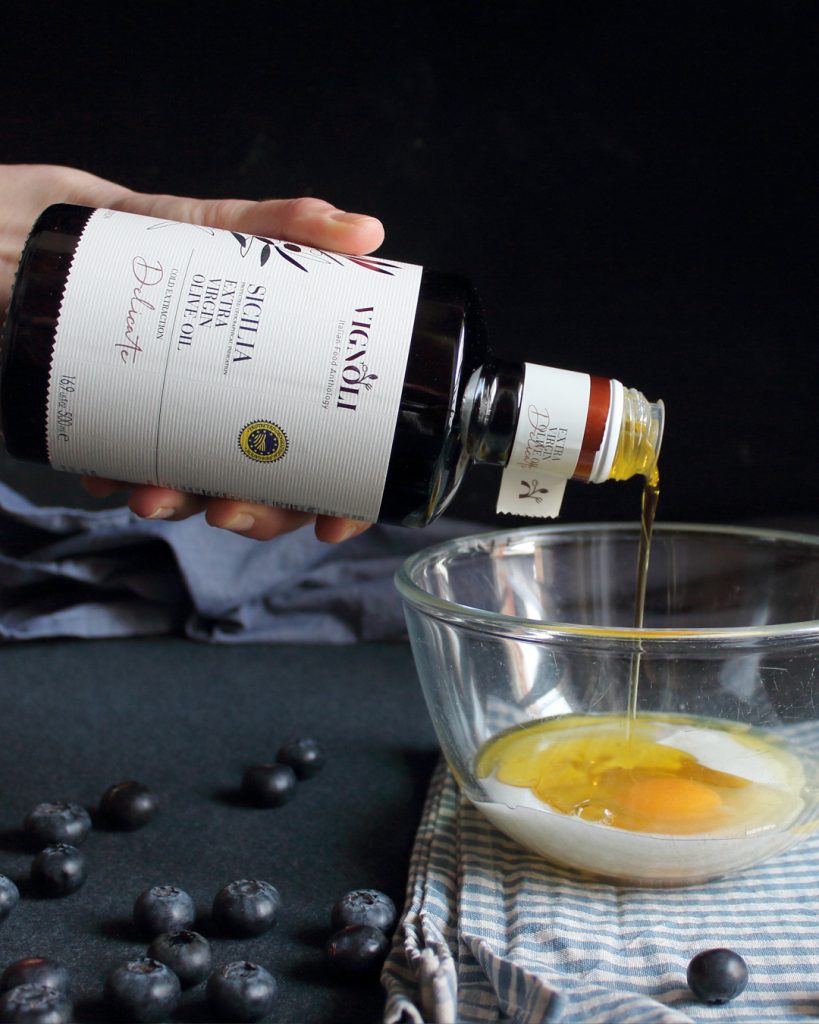 Olio extravergine Sicilia Vignoli versato nell’impasto dei pancakes con uova e mirtilli – food photography di Paola Uberti